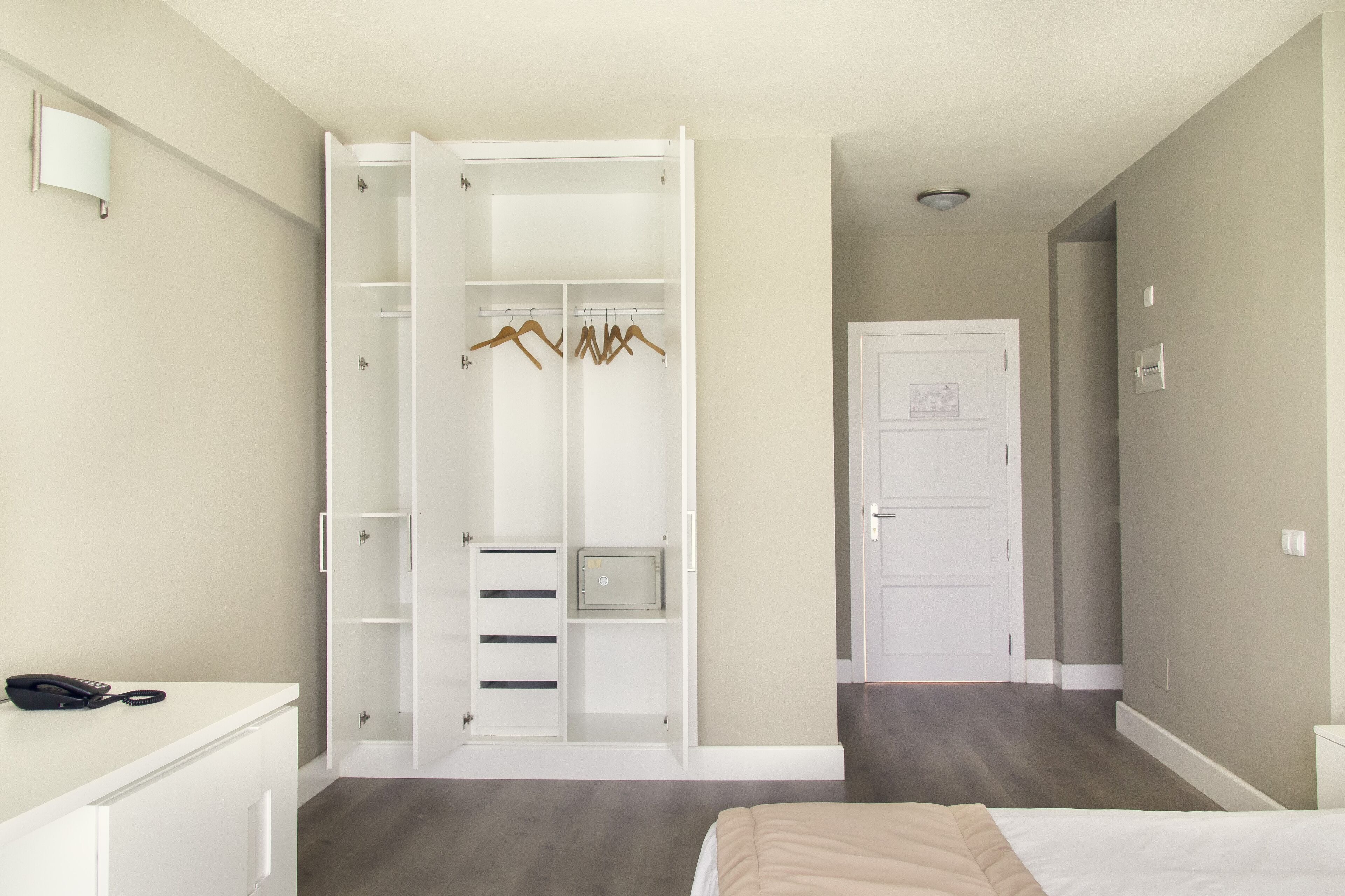 Une chambre à coucher comprenant un lit, une armoire avec espace pour suspendre des vêtements, une table de chevet et une porte donnant sur une autre pièce.