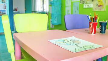 A brightly colored room with a pink table, green and purple chairs, and a wall decorated with children's drawings and notes.