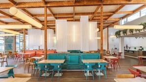 A spacious dining area with wooden beams, teal and red chairs, and long tables.