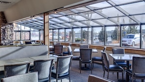 A restaurant with a glass roof, stone wall, and seating area with tables and chairs.