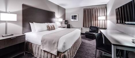 Habitación de hotel con cama, mesita de noche, lámpara, silla, escritorio y un espejo grande.