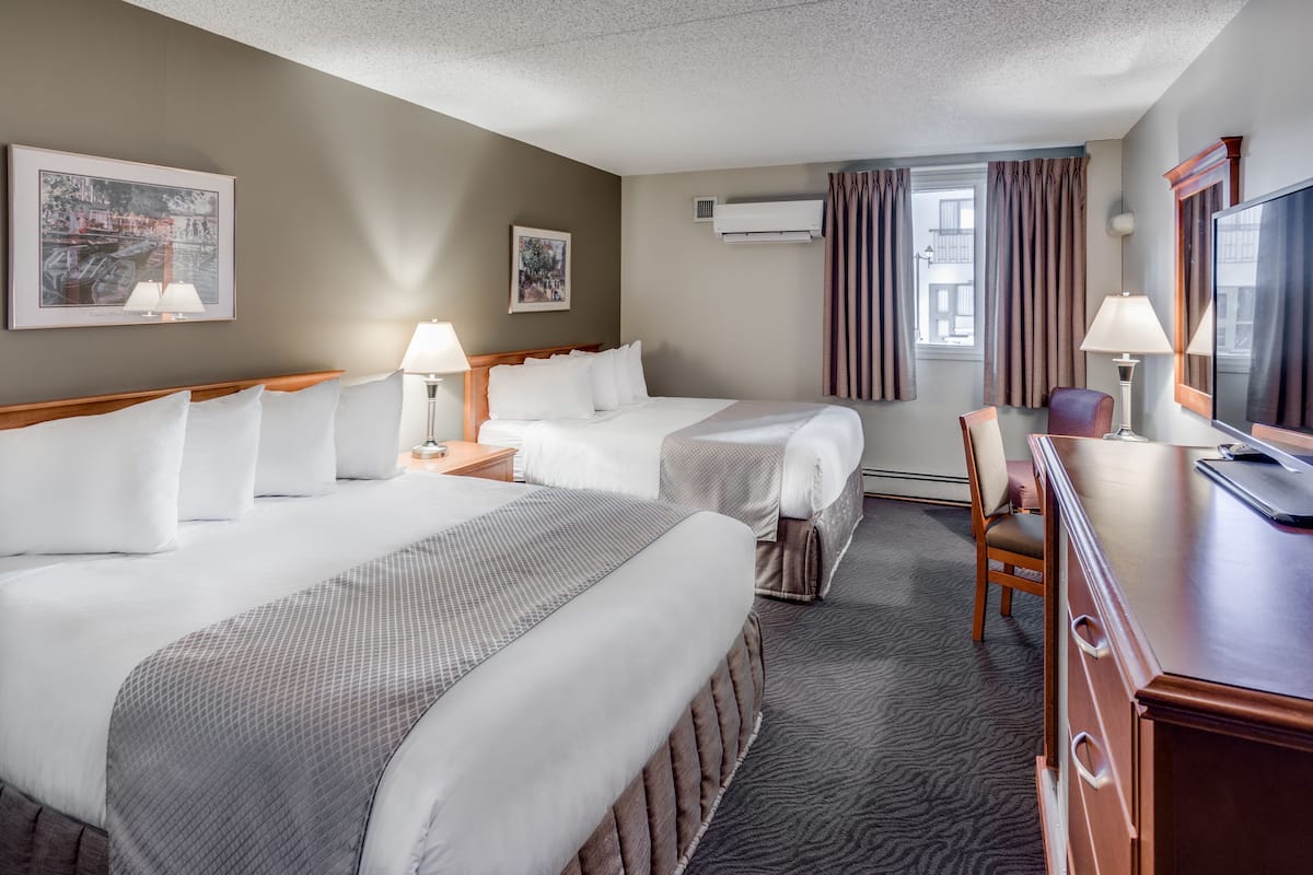 A hotel room with two beds, a desk, a chair, a TV, and a window with curtains.