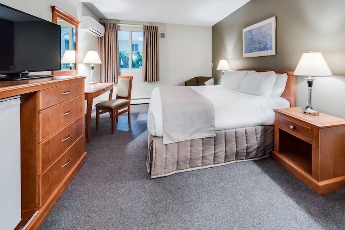 A hotel room with a bed, a desk, a television, a chair, and a window with curtains.