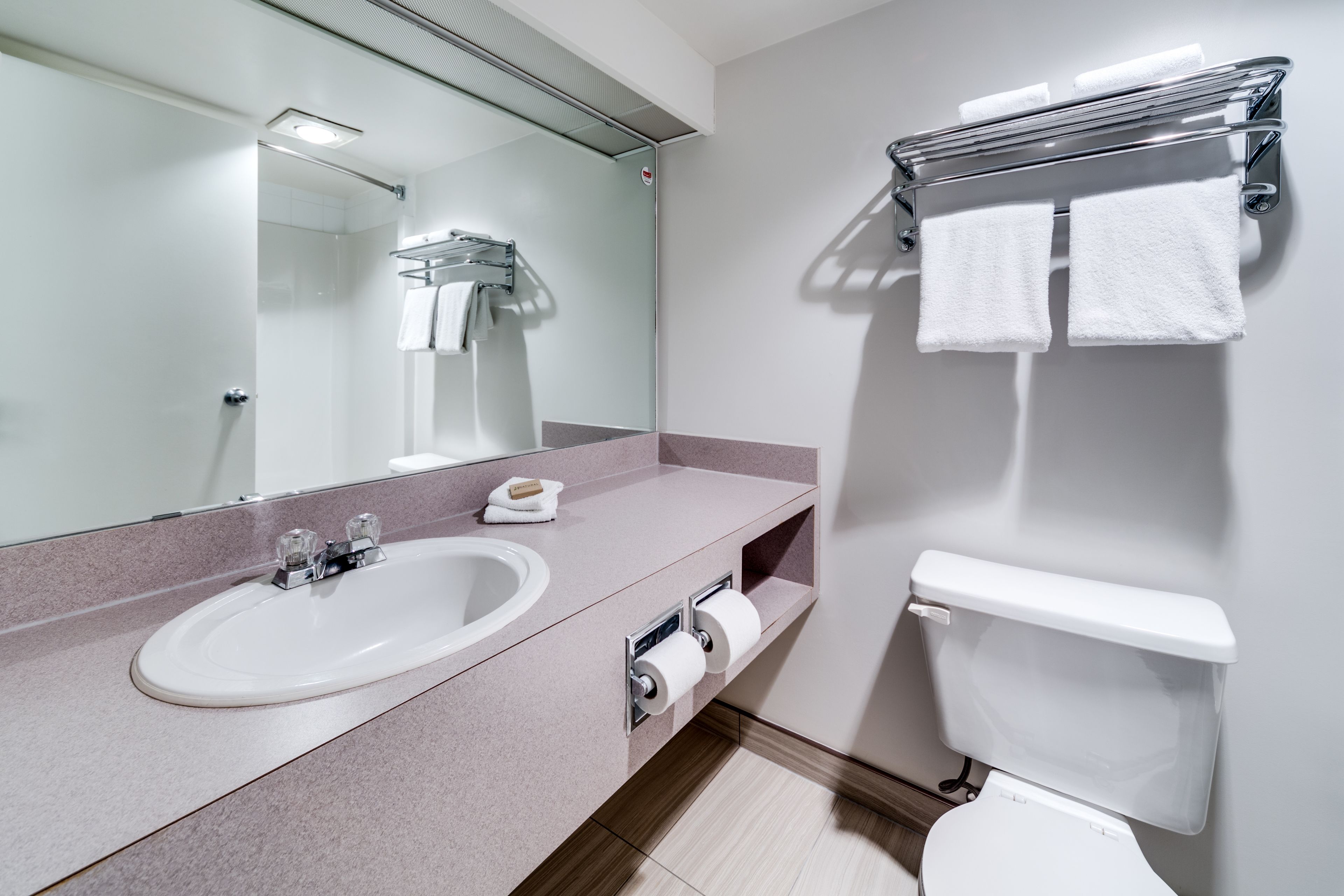 A modern bathroom with a sink, mirror, toilet, and towel rack.