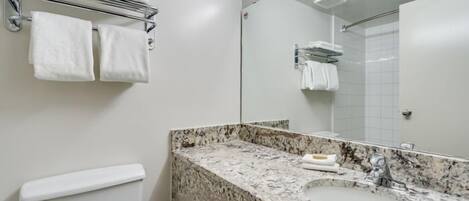 Un baño con lavamanos de mármol, un perchero con toallas, un inodoro y un espejo.