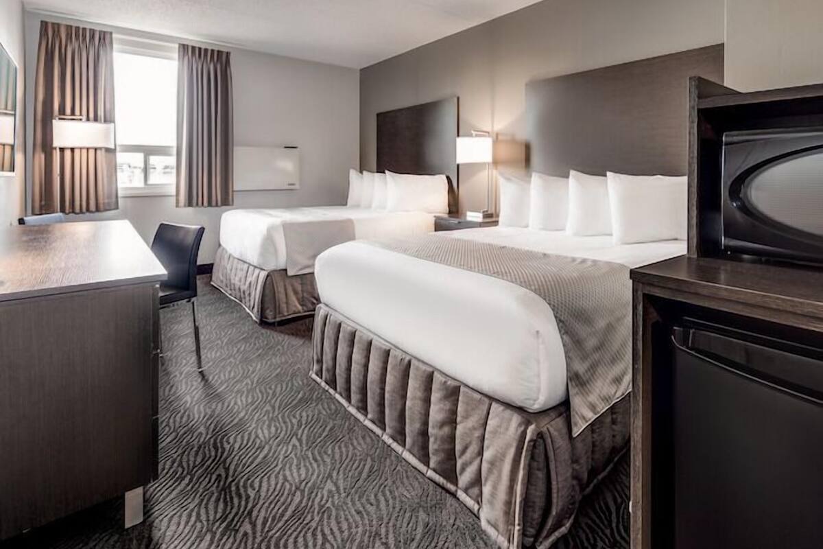 A hotel room with two beds, a desk, a television, and a lamp.