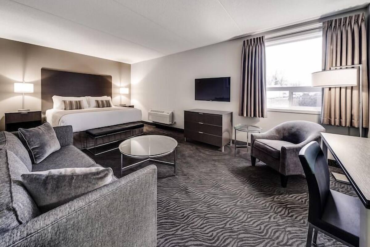 A hotel room with a bed, a sofa, a desk, a chair, a TV, and a window with curtains.