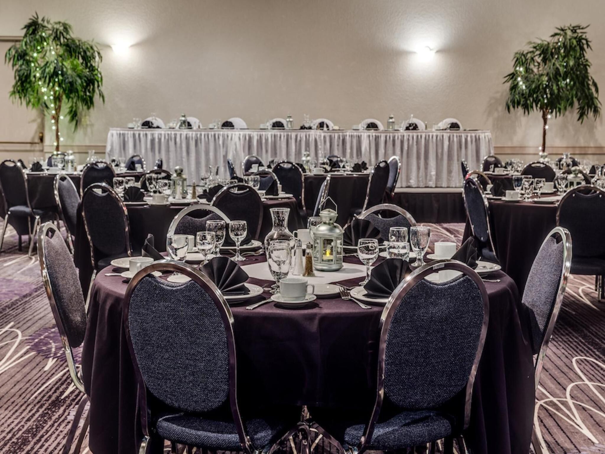 Une salle de banquet avec des tables rondes dressées pour le repas, chacune étant agrémentée de chaises et de couverts.