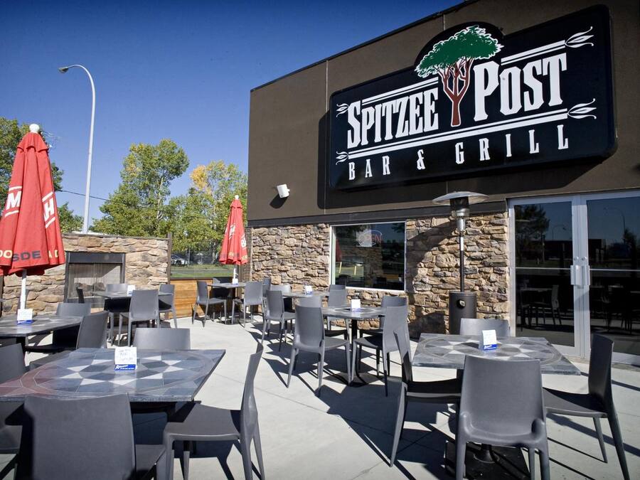 An outdoor seating area with tables and chairs, a stone wall, and a sign for Spitzee Post Bar & Grill.