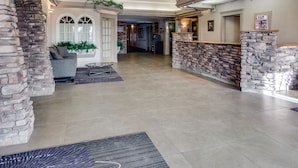 A spacious lobby with a stone reception desk, a seating area with a sofa and armchairs, and a large rug on the floor.