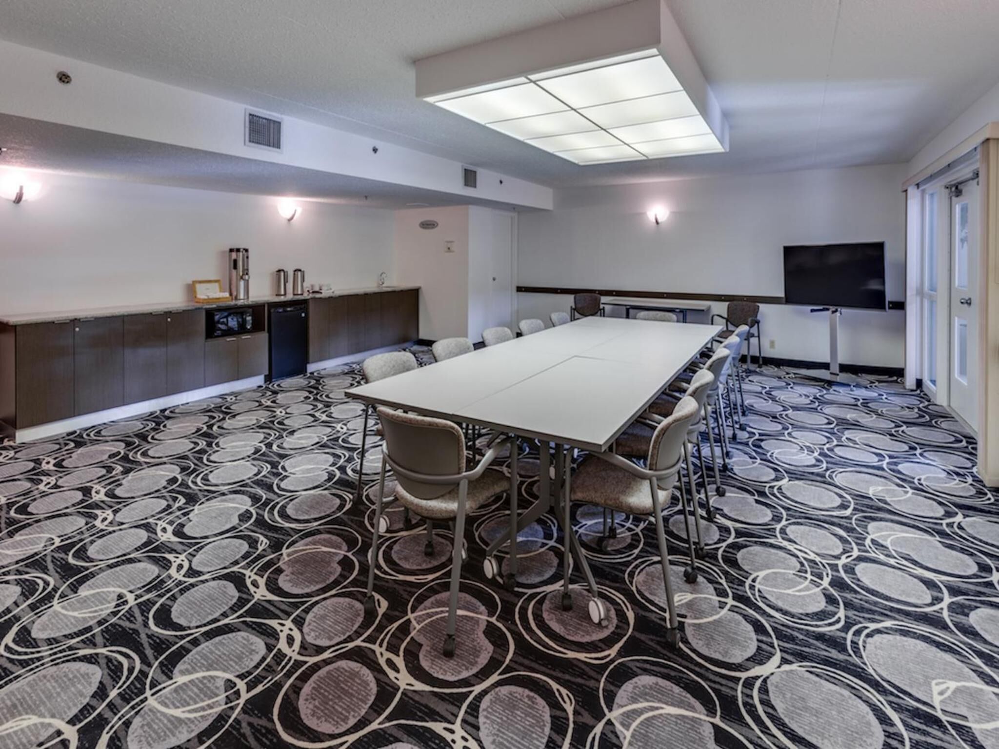 A conference room with a long table, chairs, a TV, and a patterned carpet.