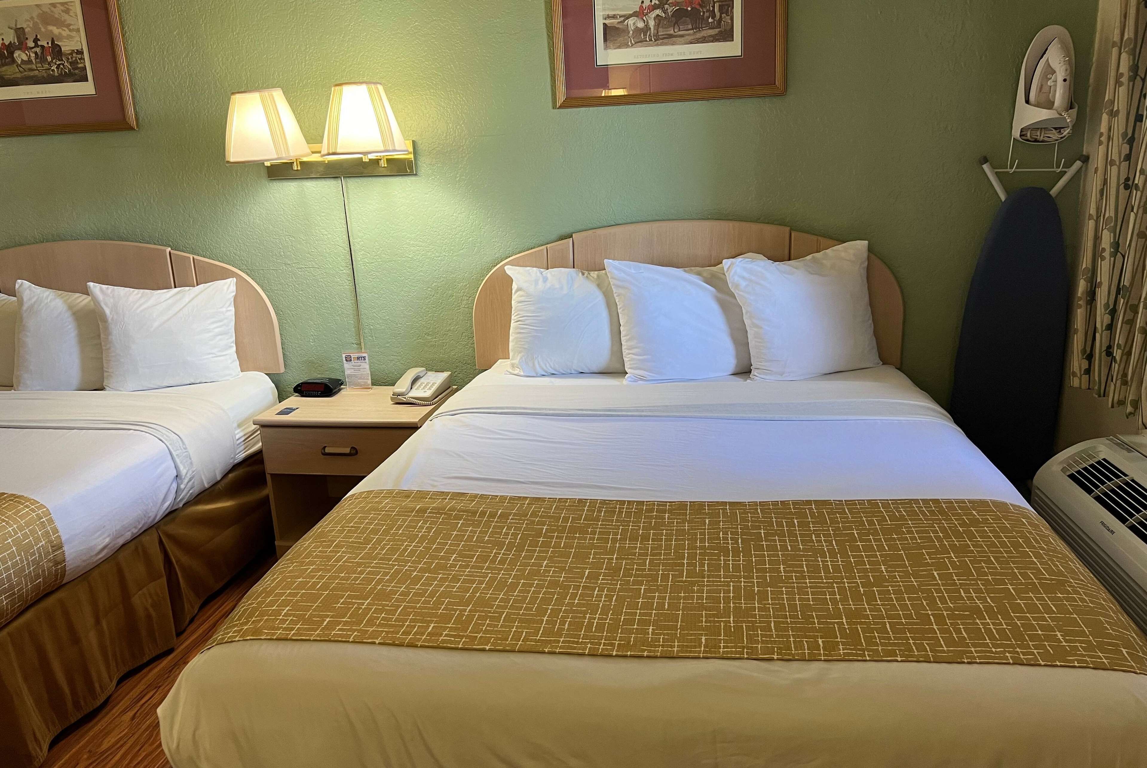A hotel room with two beds, a nightstand, a lamp, an iron, and a wall-mounted picture.