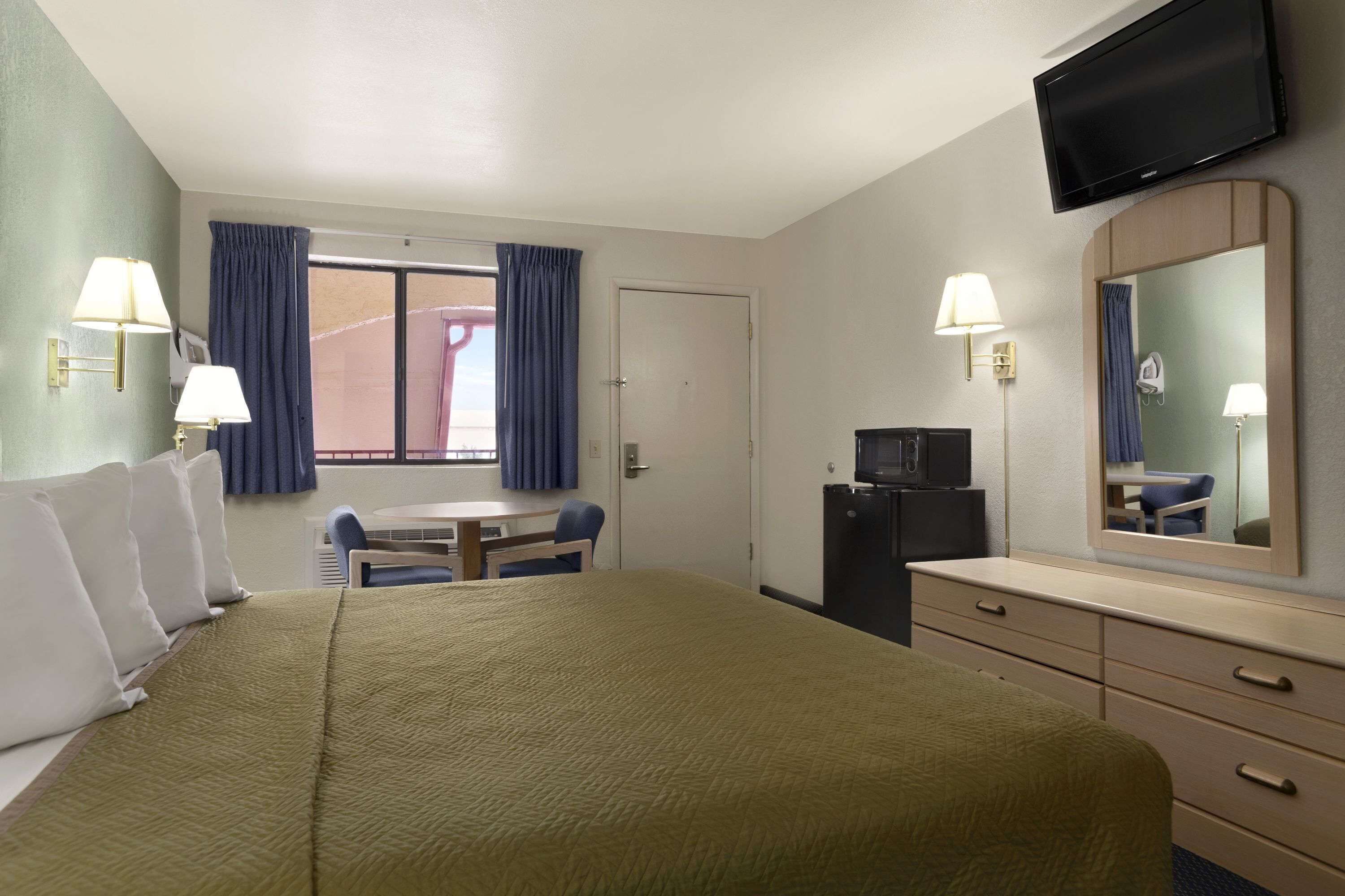 A hotel room with a bed, a desk, a chair, a dresser, a television, and a window with curtains.