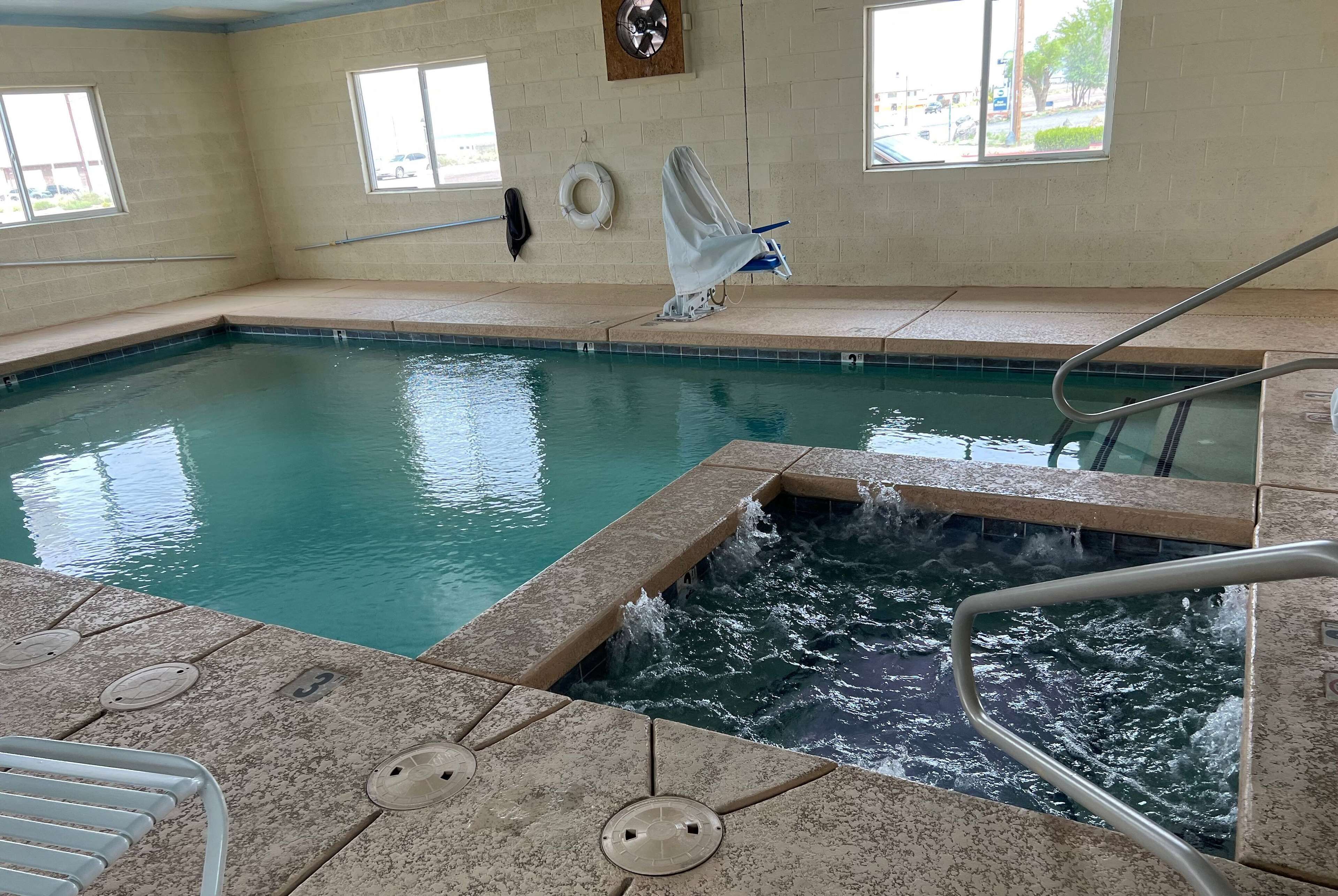 An indoor swimming pool with clear water, a small waterfall feature, and a poolside area with a lifeguard stand and a covered seating area.