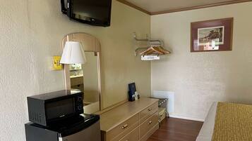 A hotel room with a microwave on a mini-fridge, a TV mounted on the wall, a dresser with drawers, a hanging coat rack, and a framed picture on the wall.