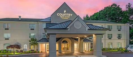 Edificio de Country Inn & Suites by Radisson con una entrada destacada y un camino de entrada ajardinado.