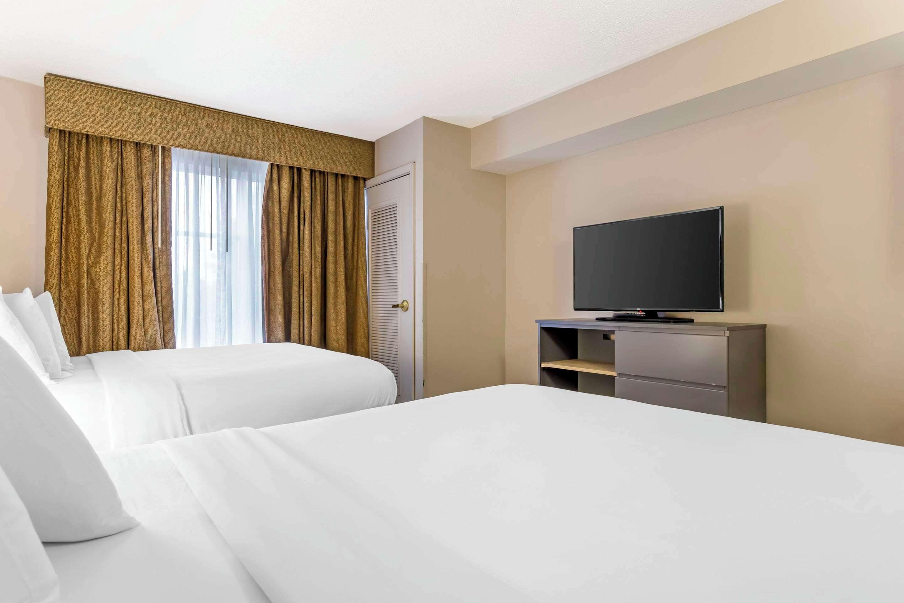 A hotel room with two beds, a television on a stand, and a window with curtains.