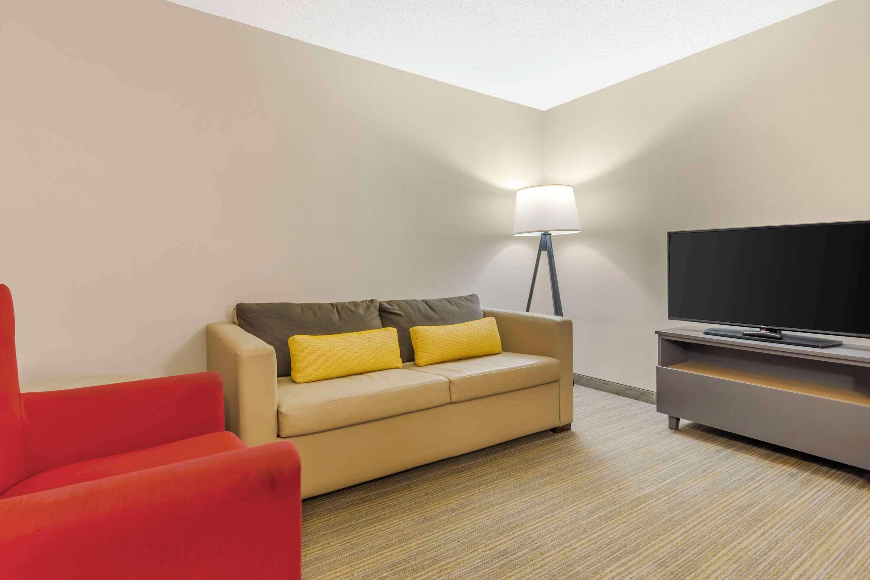 A modern living room with a beige sofa, a red armchair, a flat-screen TV, and a floor lamp.
