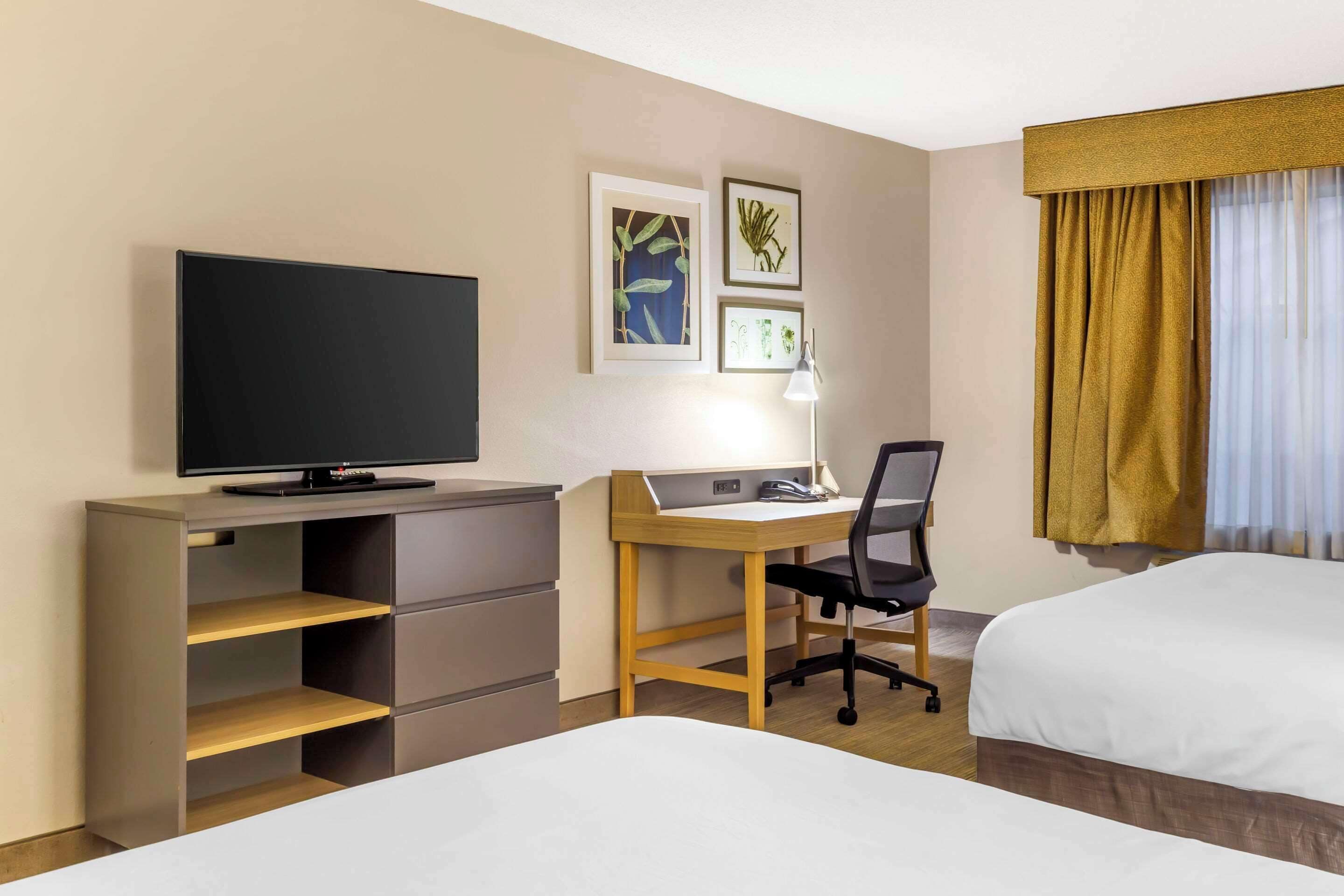 A hotel room with a bed, a desk with a chair, a television, and a bookshelf.