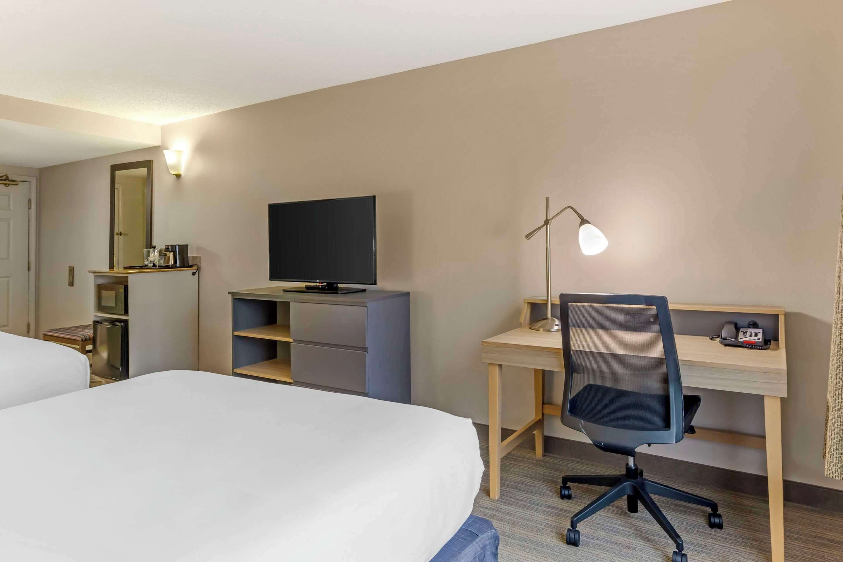 A hotel room with two beds, a desk with a computer, a TV, and a desk lamp.