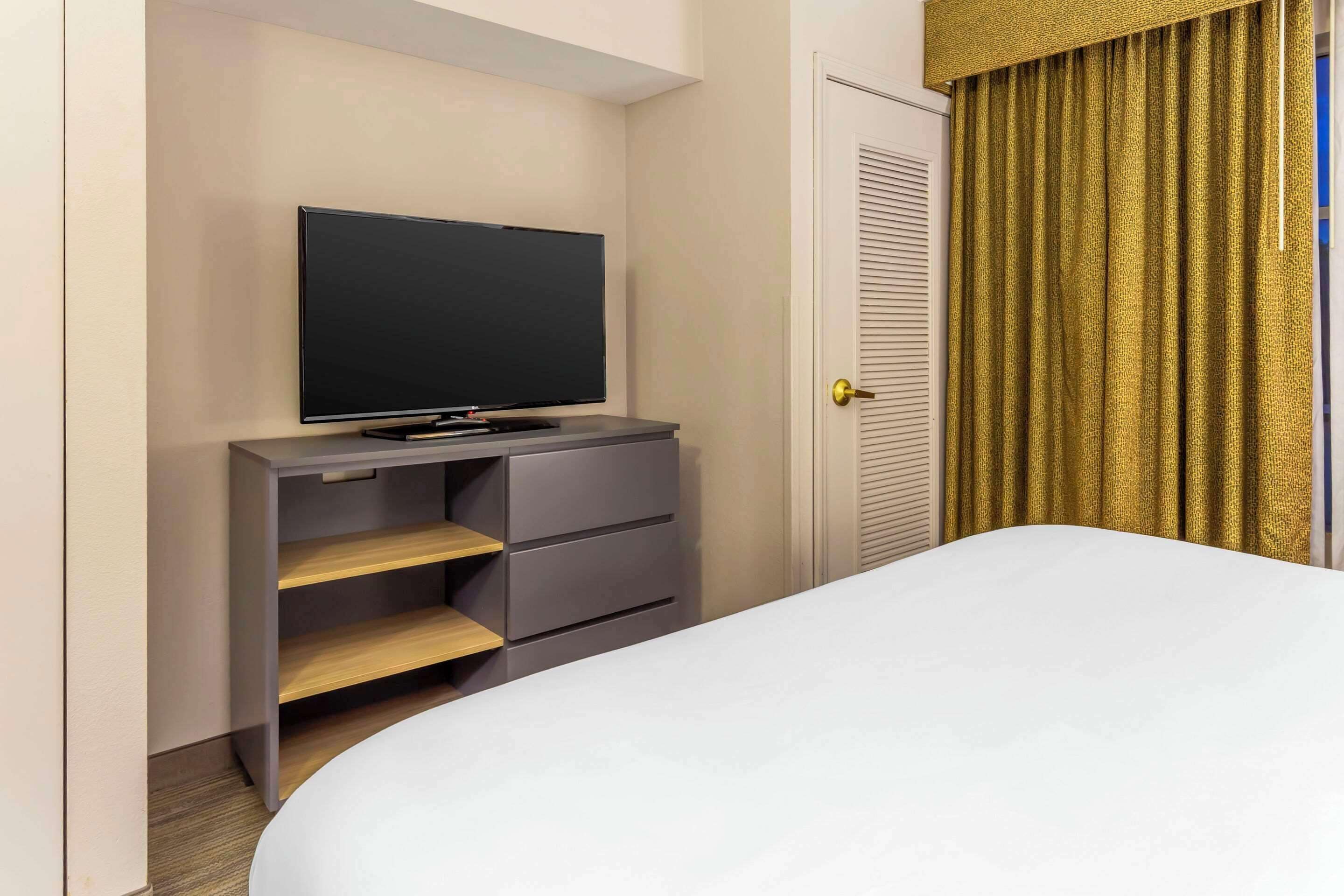 A hotel room with a bed, a television on a grey cabinet, and a door with golden curtains.
