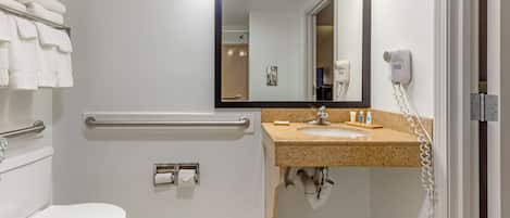 Un baño moderno con inodoro, barandilla, lavamanos y espejo.