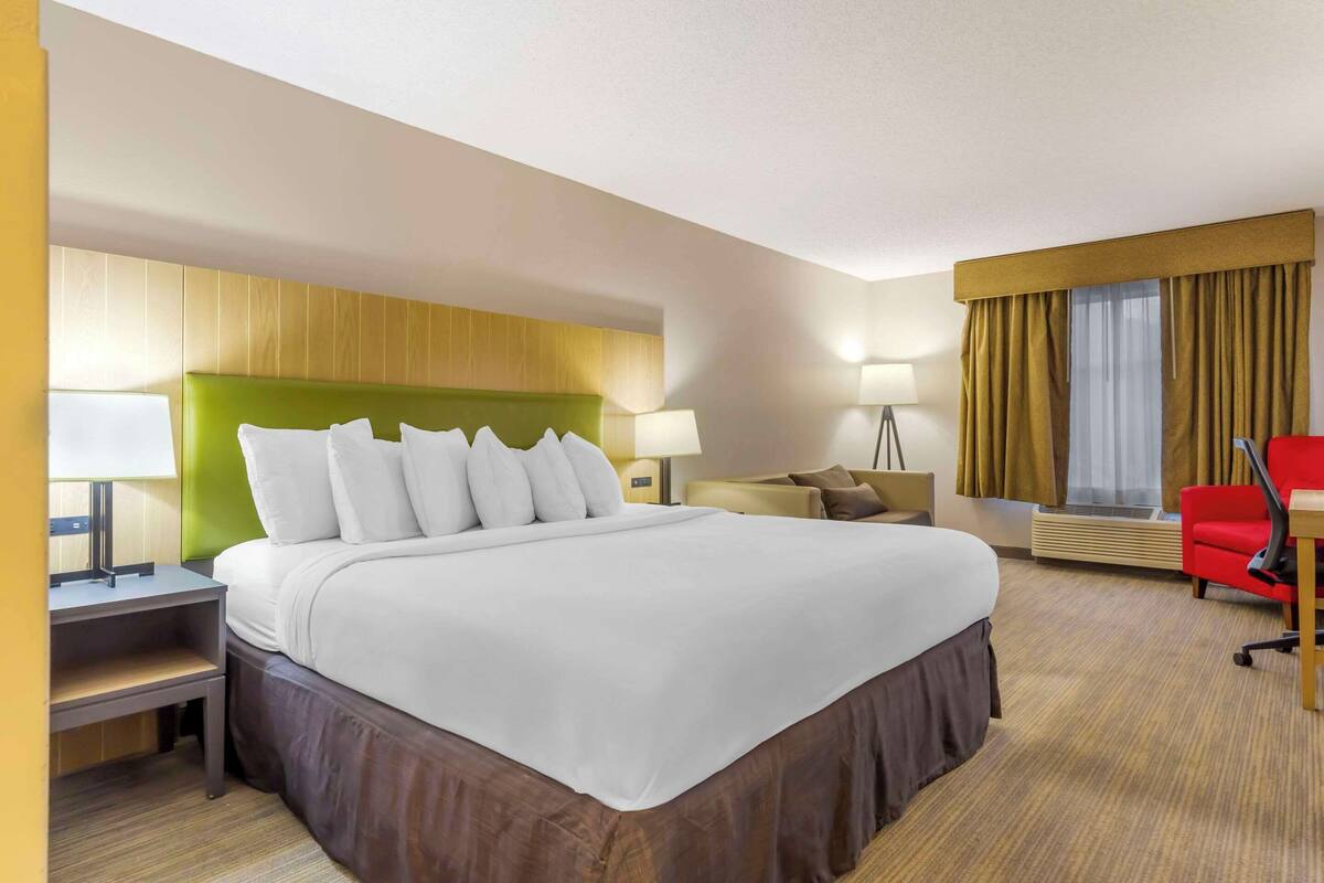 Una habitación de hotel con una cama grande, un escritorio, una silla y una ventana con cortinas.