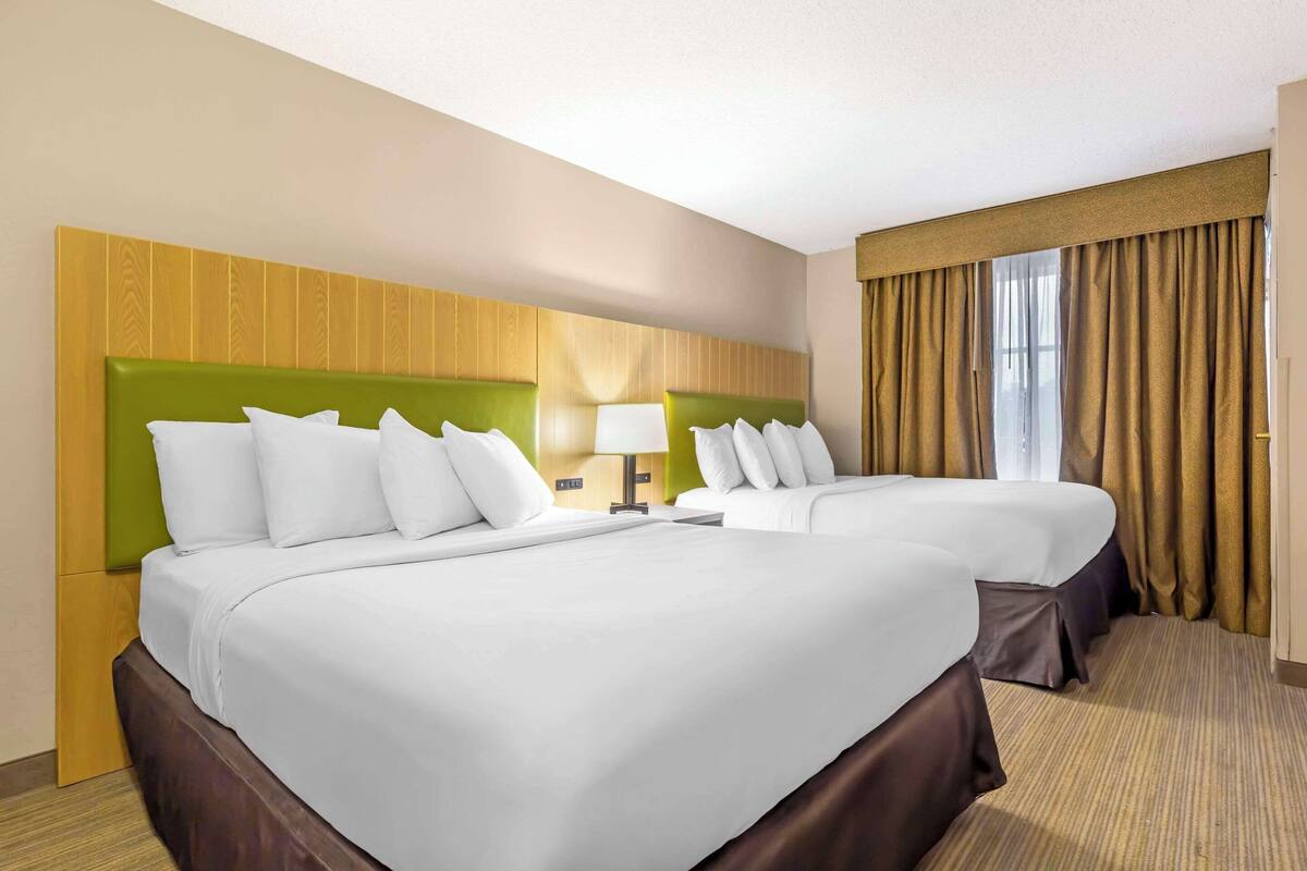 Habitación de hotel con dos camas, cabecero de madera, una lámpara y una ventana con cortinas.