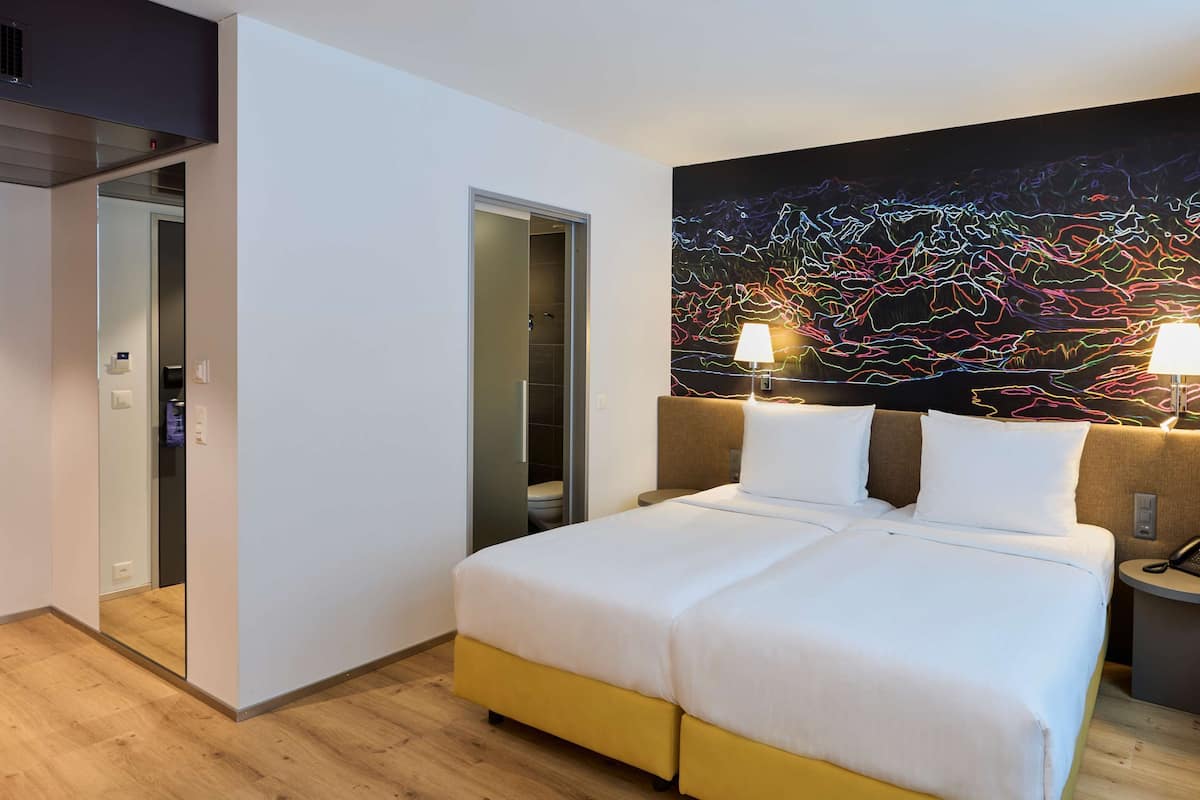 A hotel room with a double bed, bedside lamps, a nightstand with a phone, and a wall art piece.