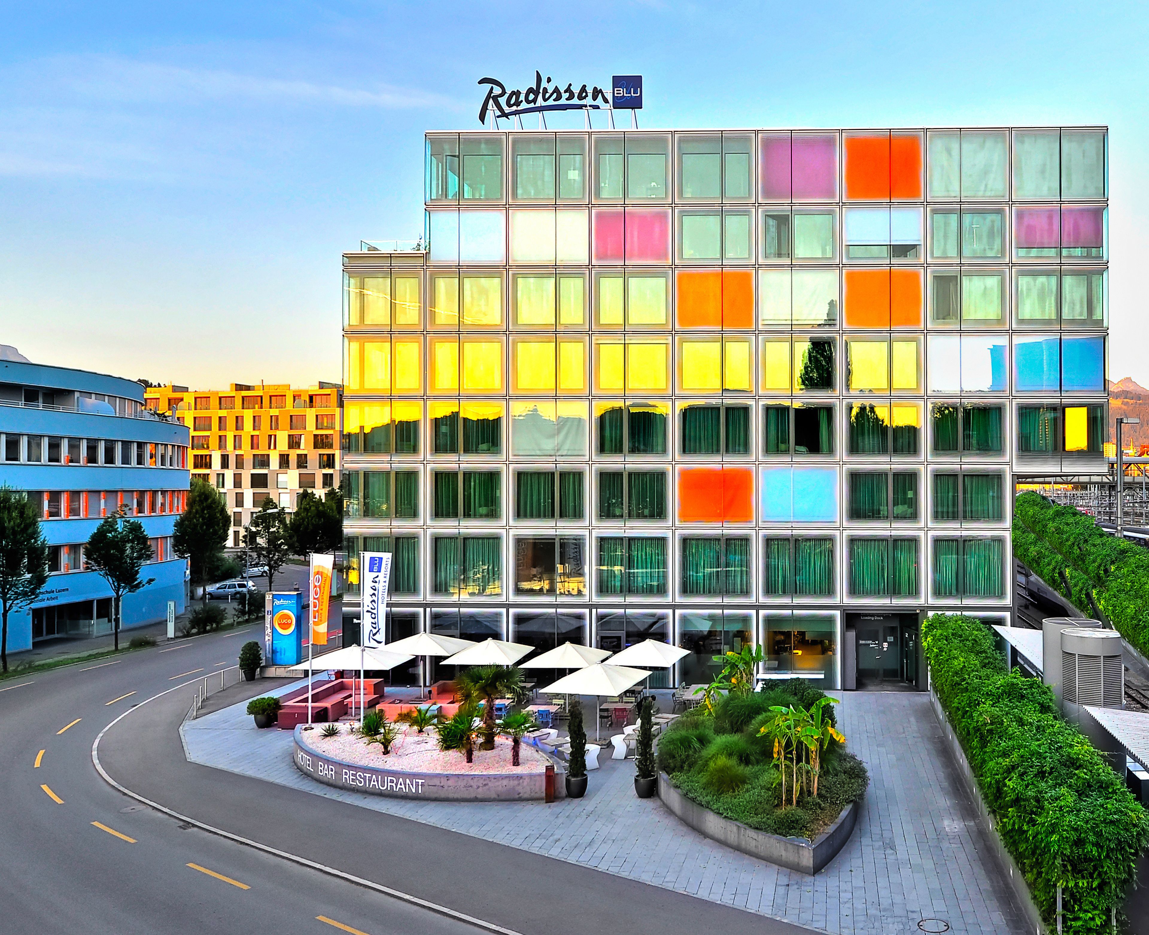 A Radisson hotel with a modern glass facade, a landscaped outdoor area with seating, and a clear sky.