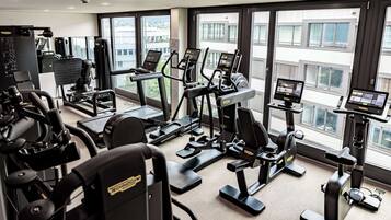 A gym with various exercise machines, large windows, and a view of buildings outside.
