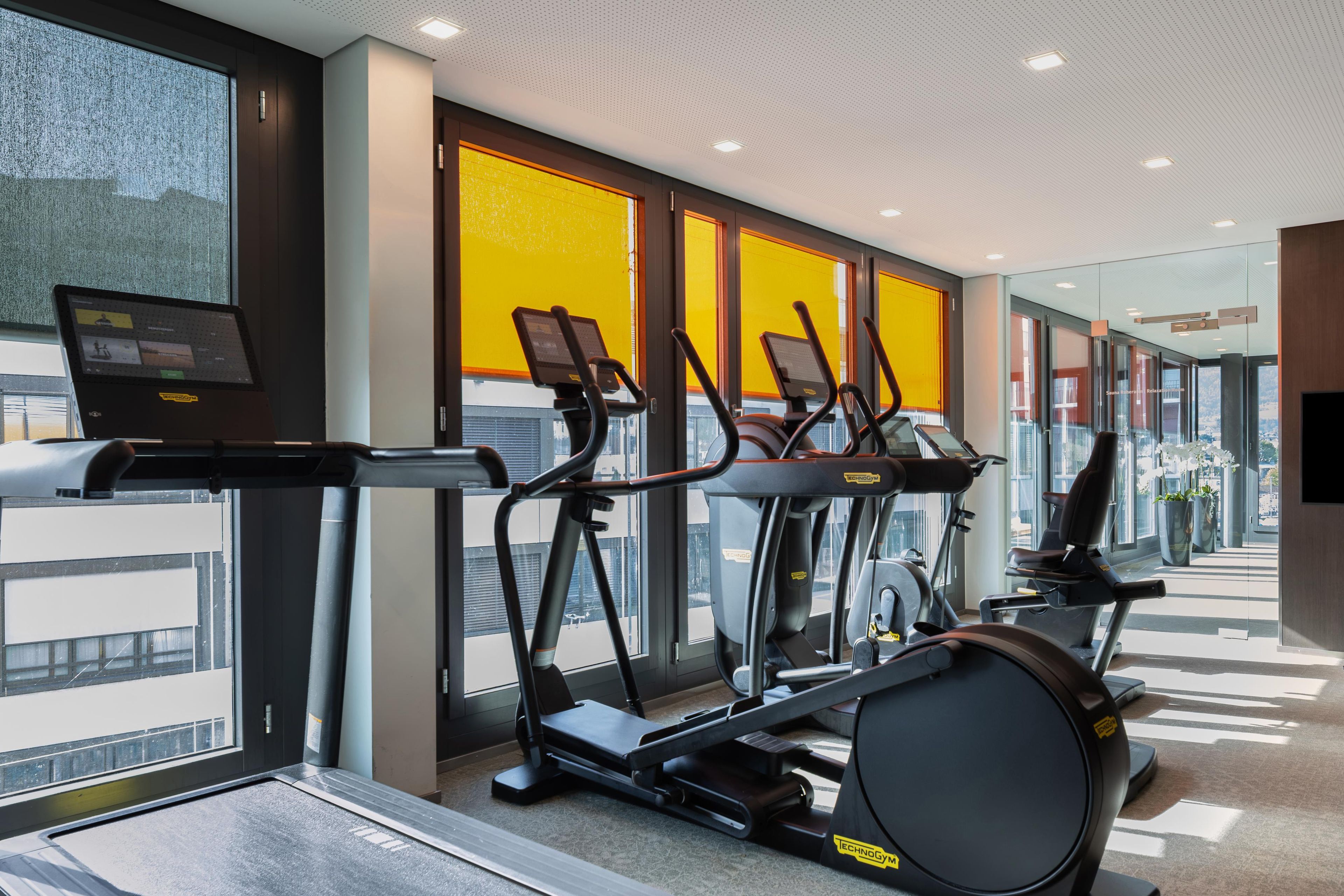 Une salle de sport équipée de tapis de course et d’un vélo d’appartement, avec de grandes fenêtres et une vue sur la ville.