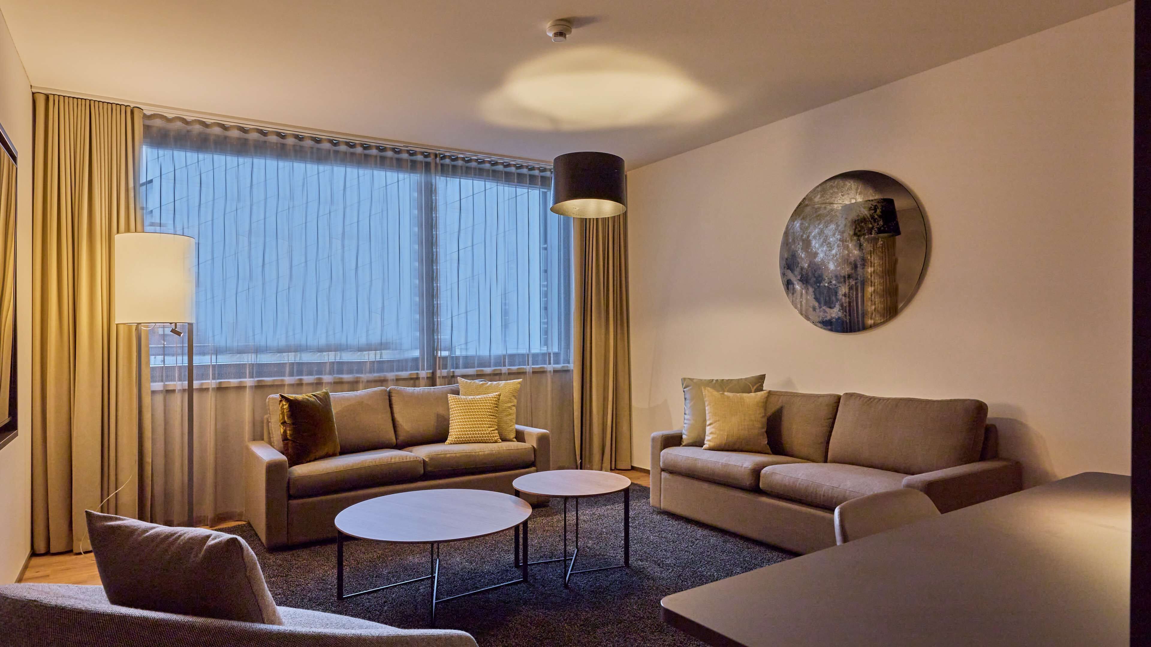 A modern hotel room with two sofas, a coffee table, and a lamp.