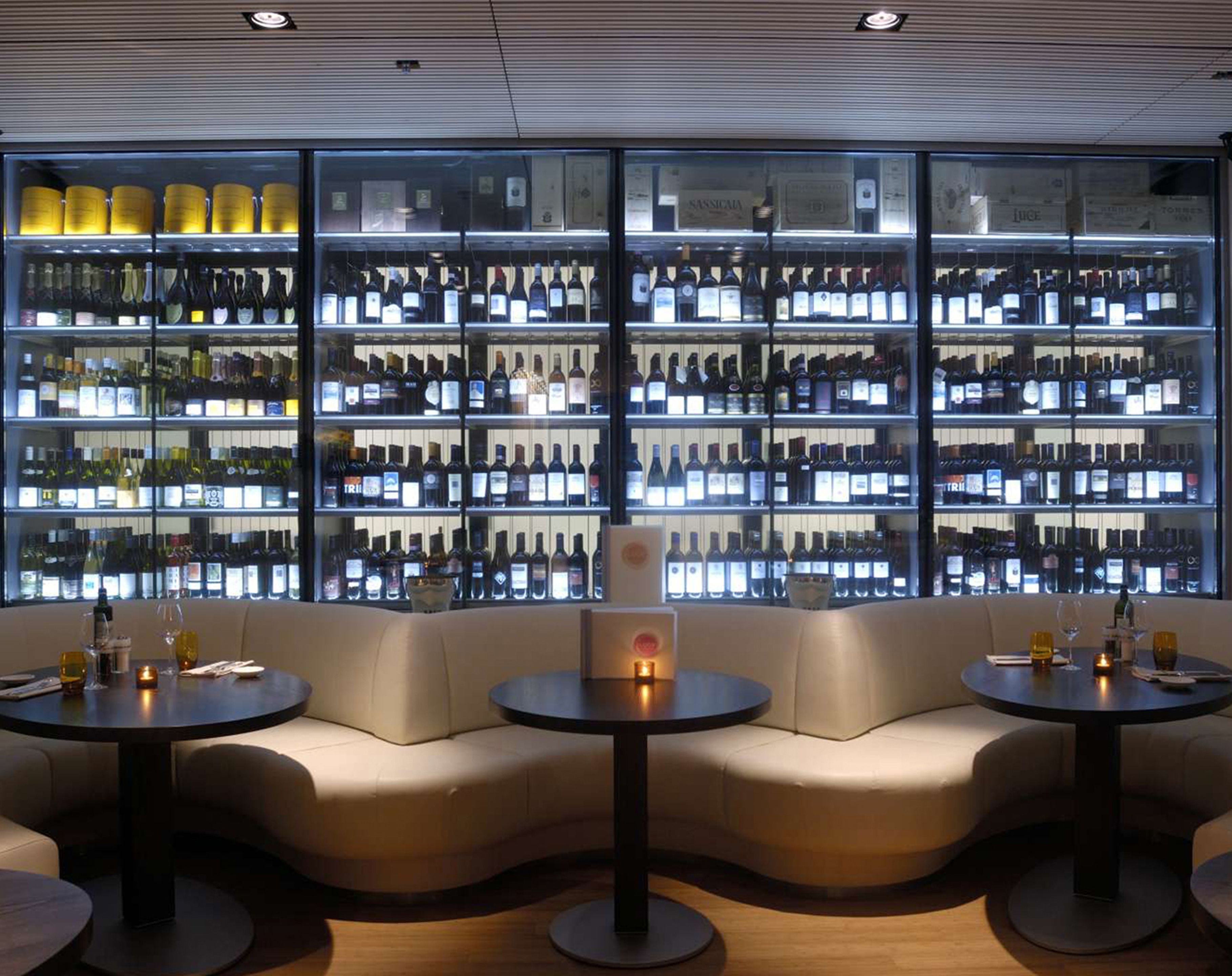 A bar area with multiple shelves of bottled beverages, cushioned seating, and round tables.
