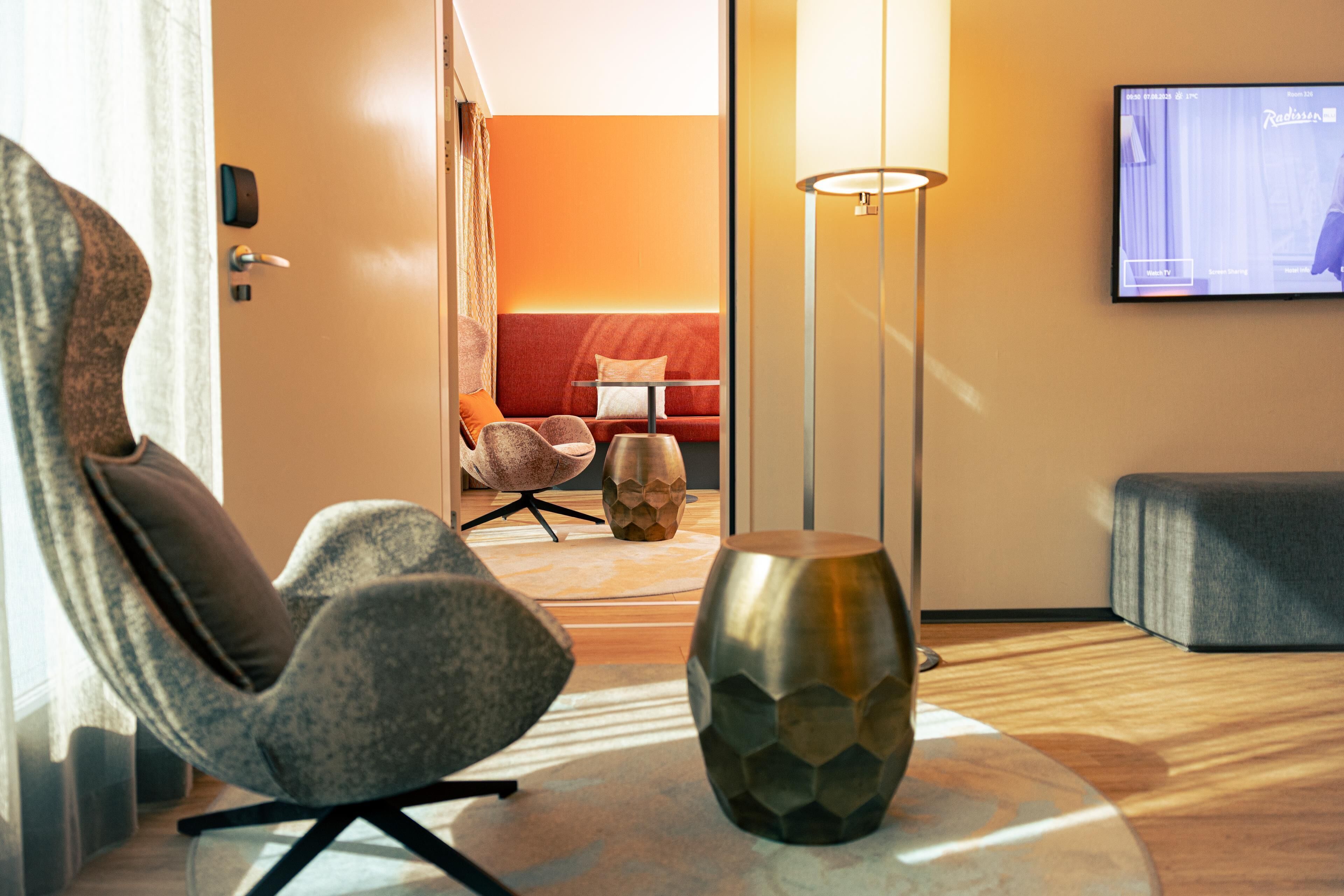 Una habitación de hotel moderna con una zona de estar acogedora, una pantalla de televisión grande y una lámpara elegante.