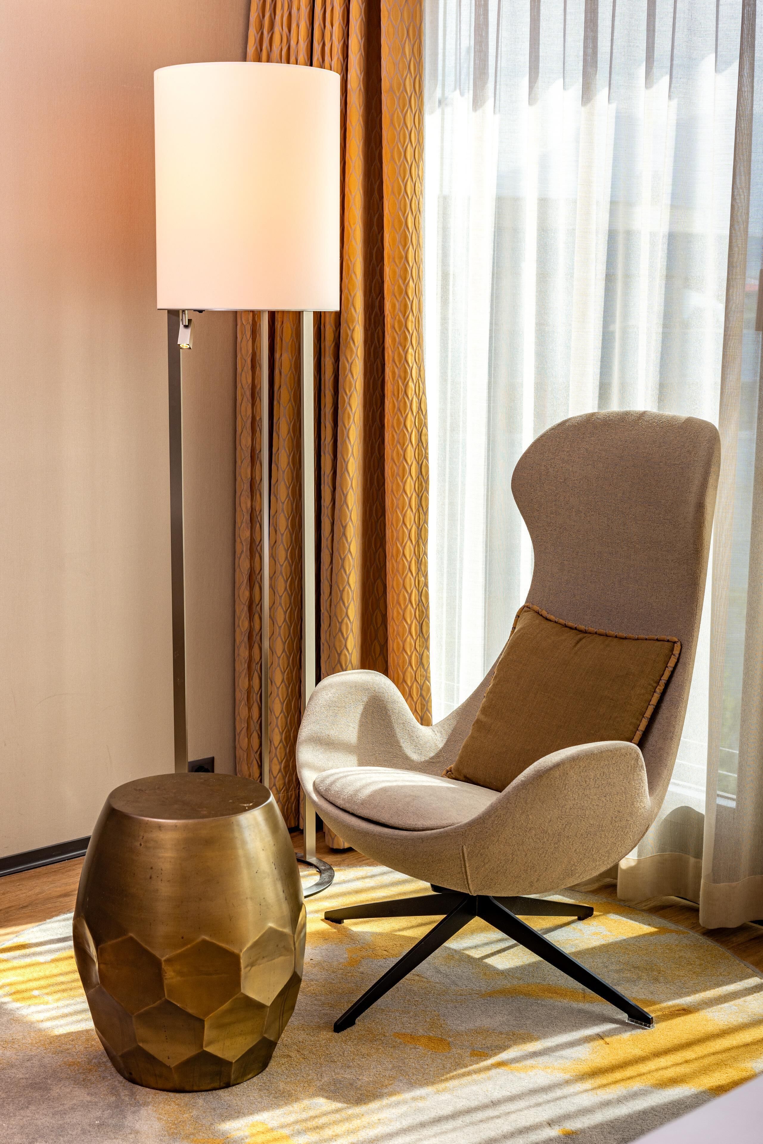 Une chambre moderne avec un fauteuil beige, une lampe sur pied et un vase décoratif en métal.