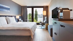 A hotel room with a large bed, a desk, a chair, a TV, and a view of the outdoors. - Radisson Blu Hotel, Lucerne (Lucerne)