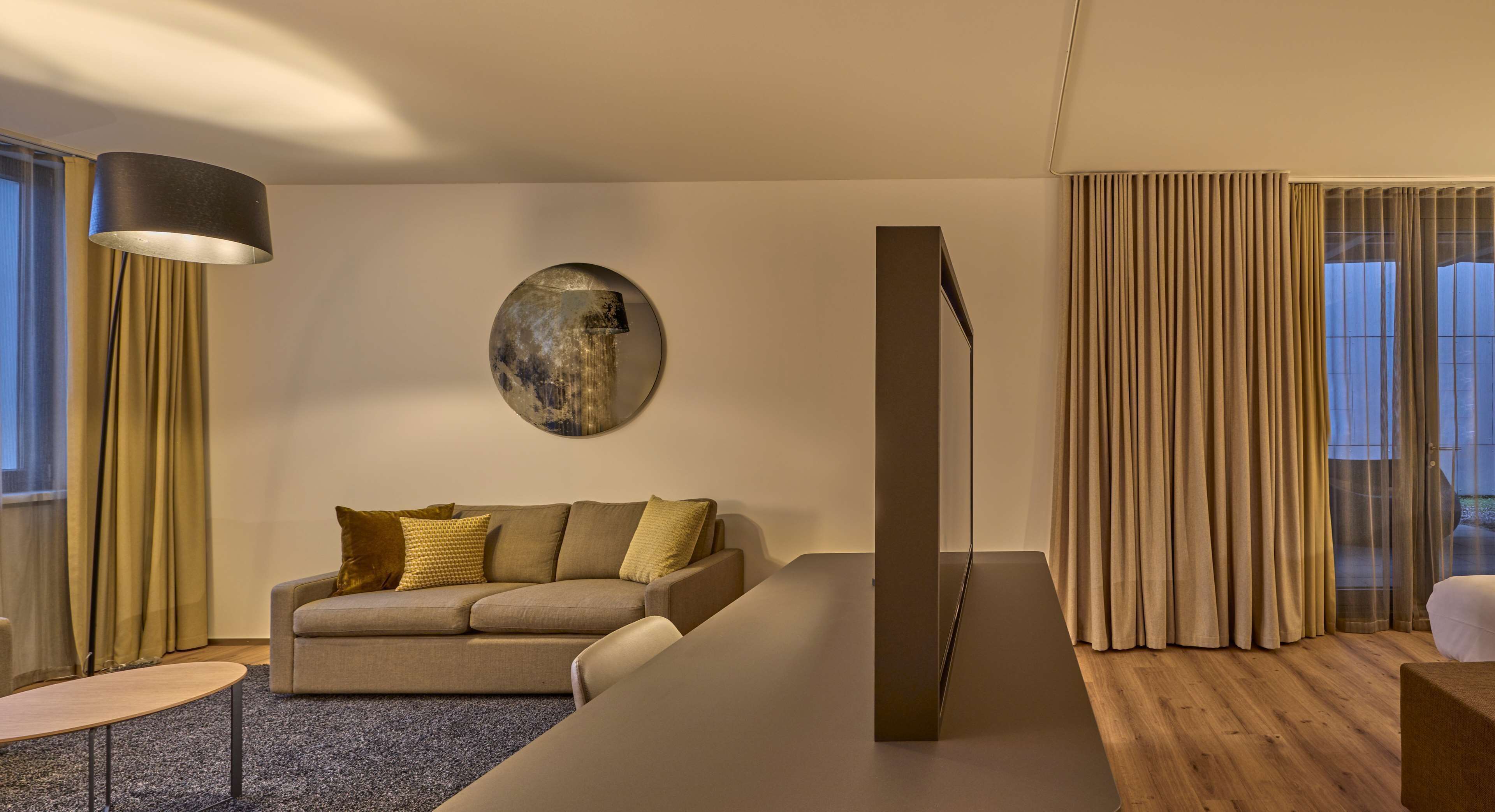 A modern living room with a sofa, a coffee table, a lamp, and a large window with curtains.