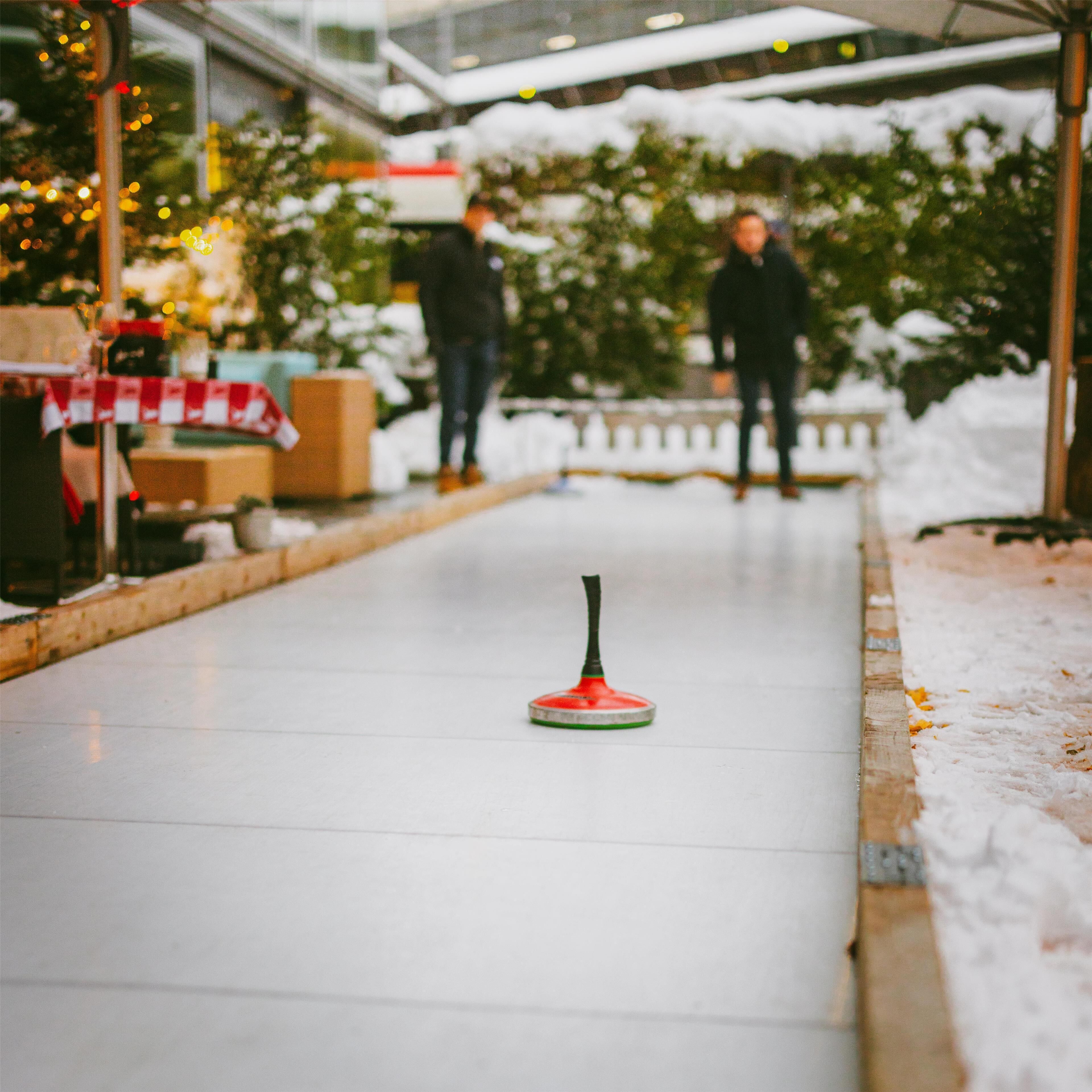 A hallway with a curling stone in the center, snow on the ground, and a Christmas tree in the background.