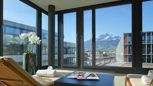 A modern hotel room with large windows, a wooden chair, a table with magazines, and a vase with white flowers. - Radisson Blu Hotel, Lucerne (Lucerne)