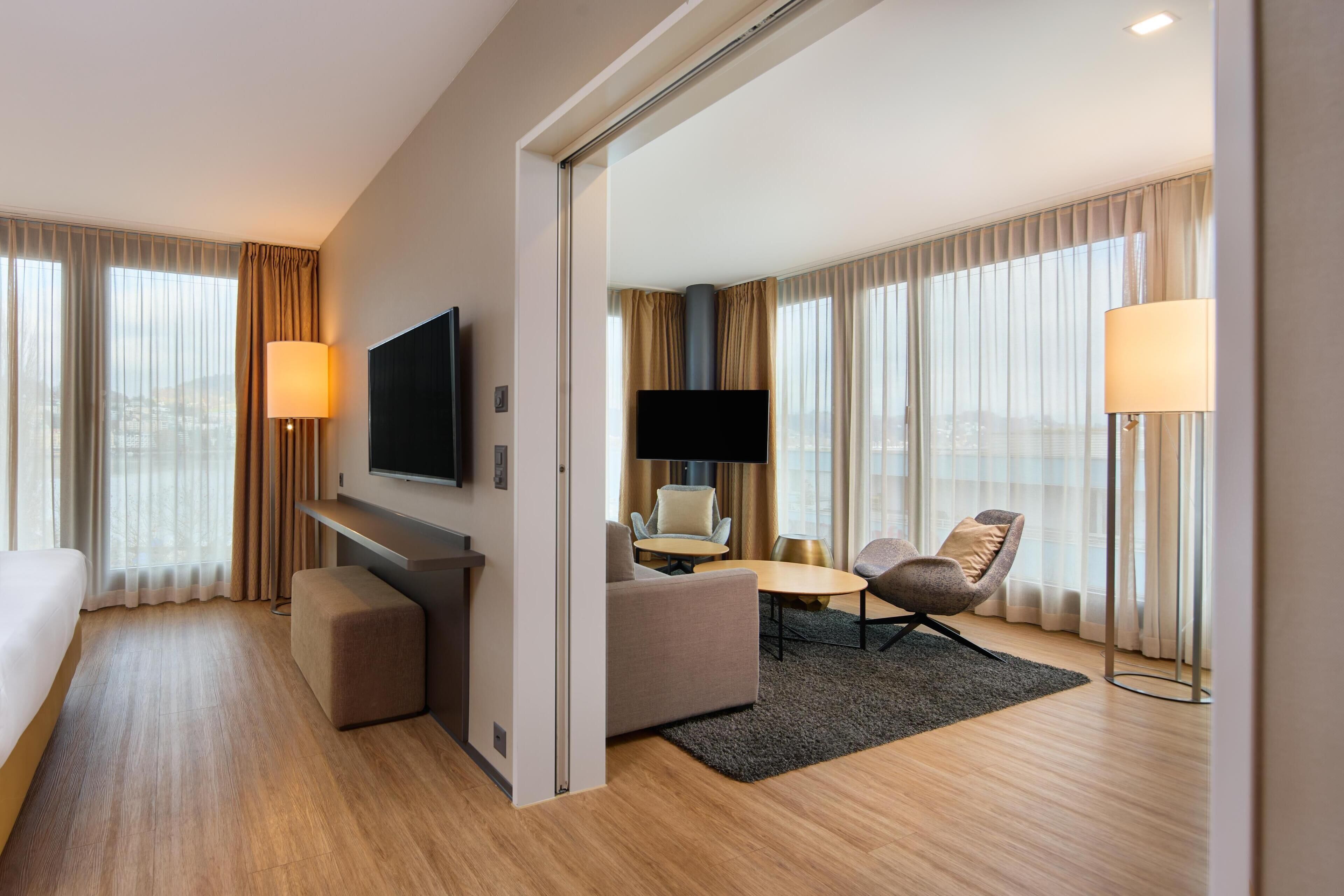 A modern hotel room with a large bed, a sofa, a TV, and a desk.