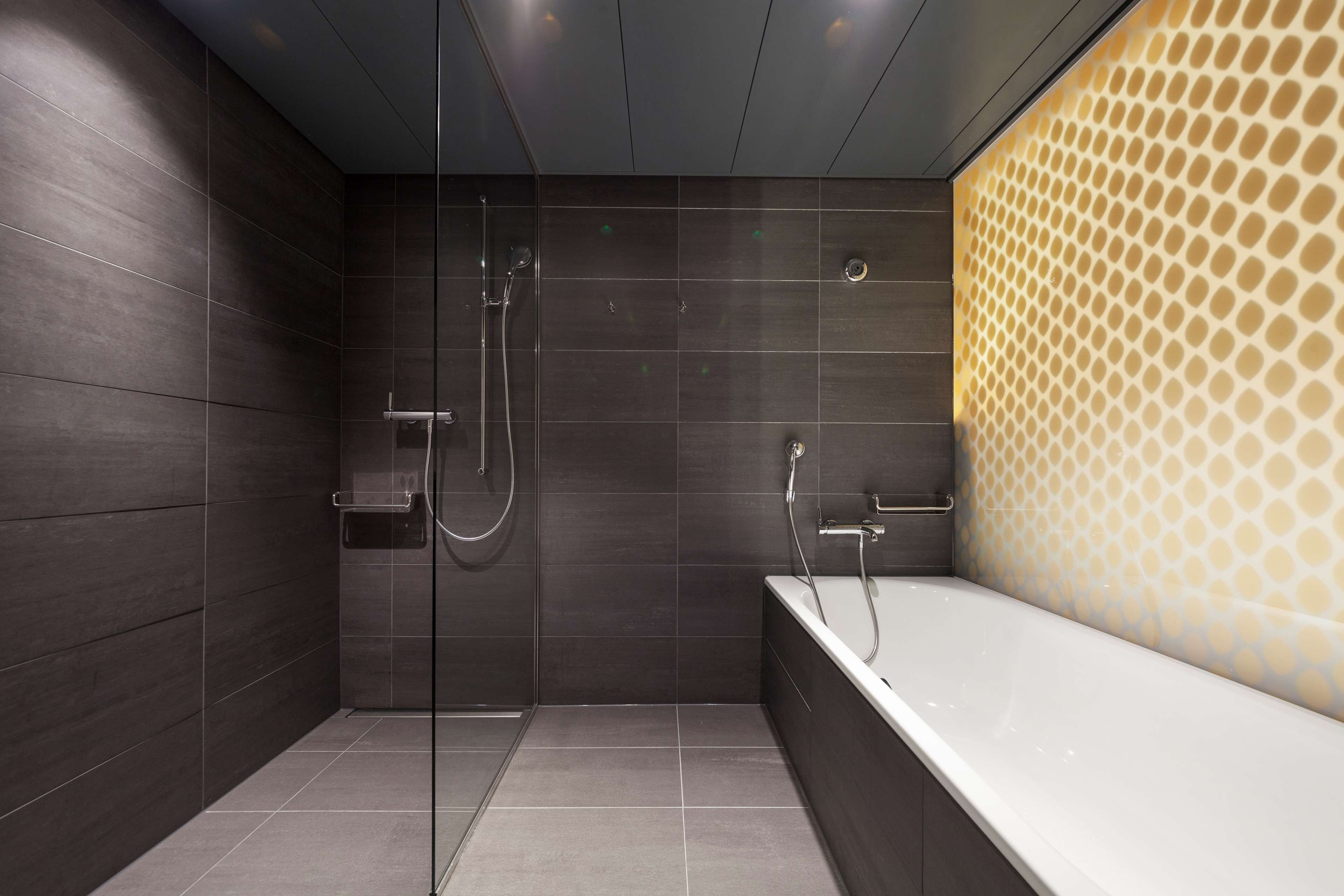 Un baño moderno con cabina de ducha de vidrio, una bañera independiente y paredes cubiertas de baldosas oscuras.