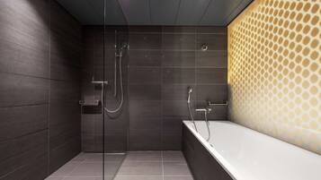 Un baño moderno con cabina de ducha de vidrio, una bañera independiente y paredes cubiertas de baldosas oscuras.