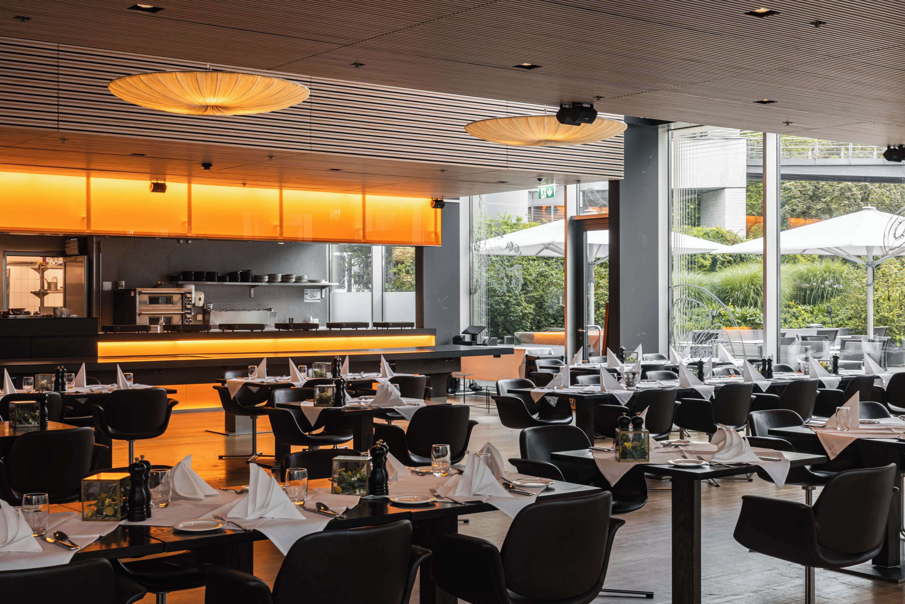 Um restaurante moderno com ampla área de refeições, grandes janelas e cozinha à vista.