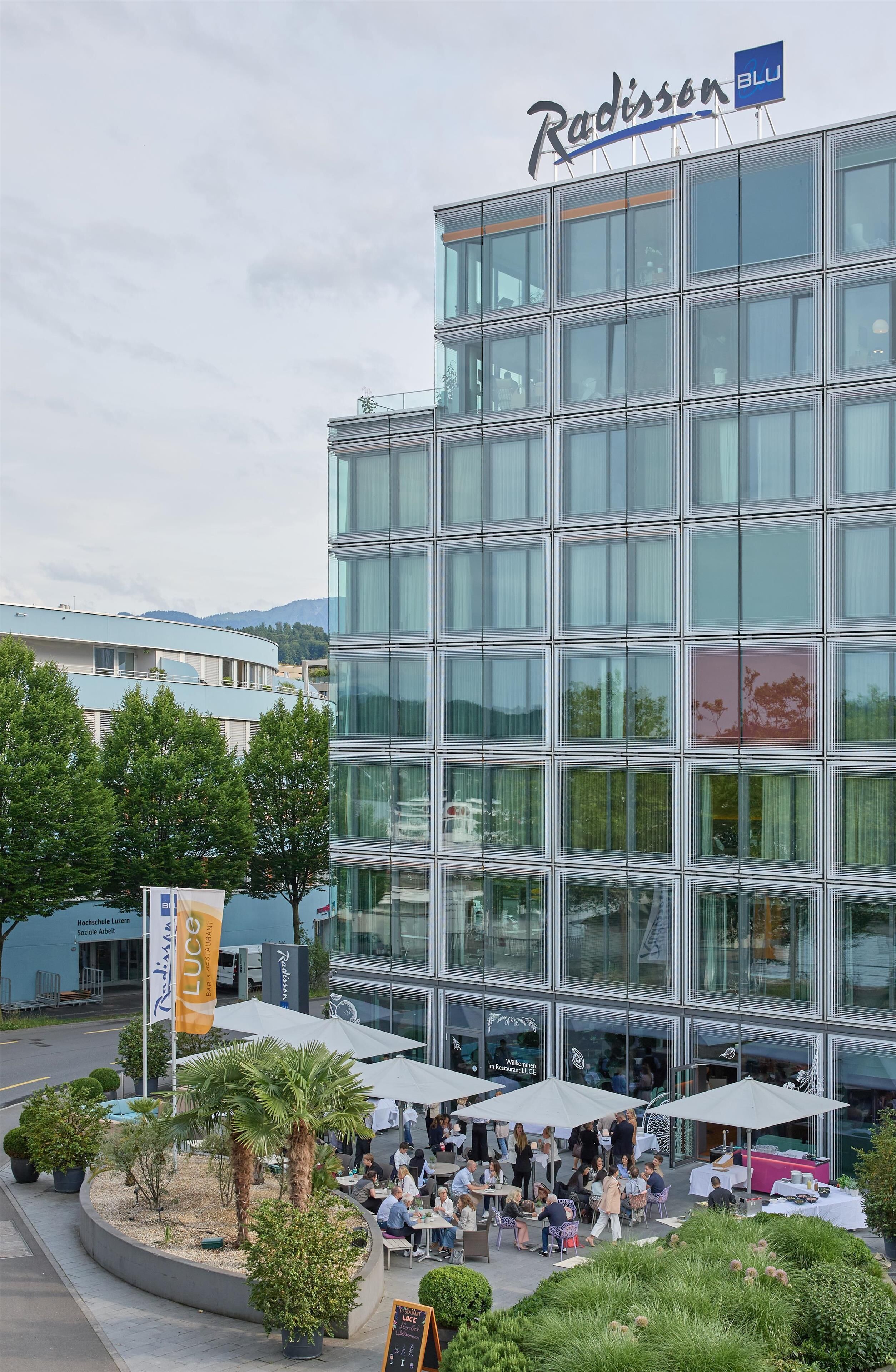 Ein Radisson BLU Hotel mit moderner Glasfassade, Außenbereich mit Sonnenschirmen und einem angelegten Garten.