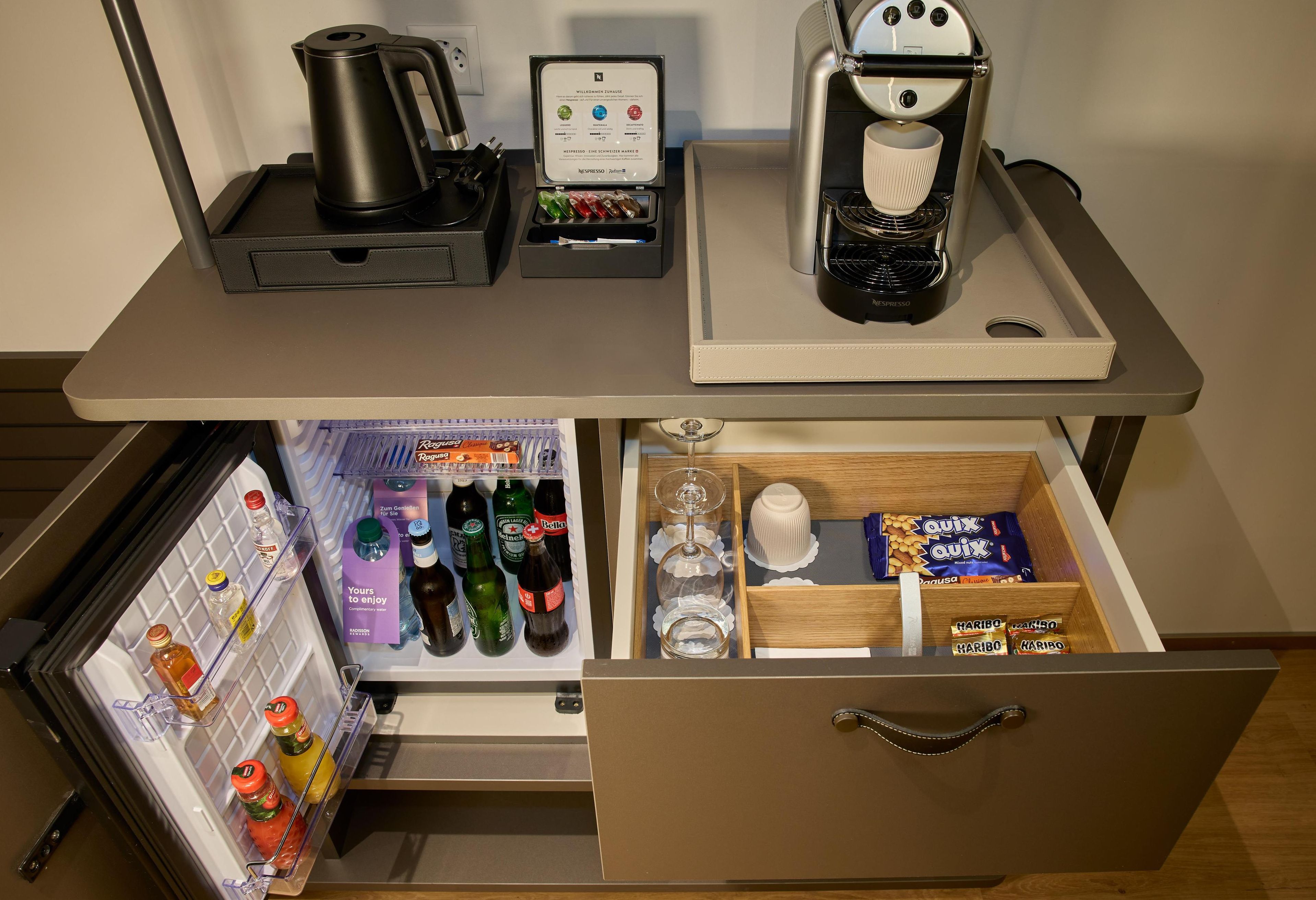 Une petite cuisine équipée d’une machine à café, d’une bouilloire, d’un réfrigérateur à vin et d’un réfrigérateur rempli de boissons et d’en-cas.