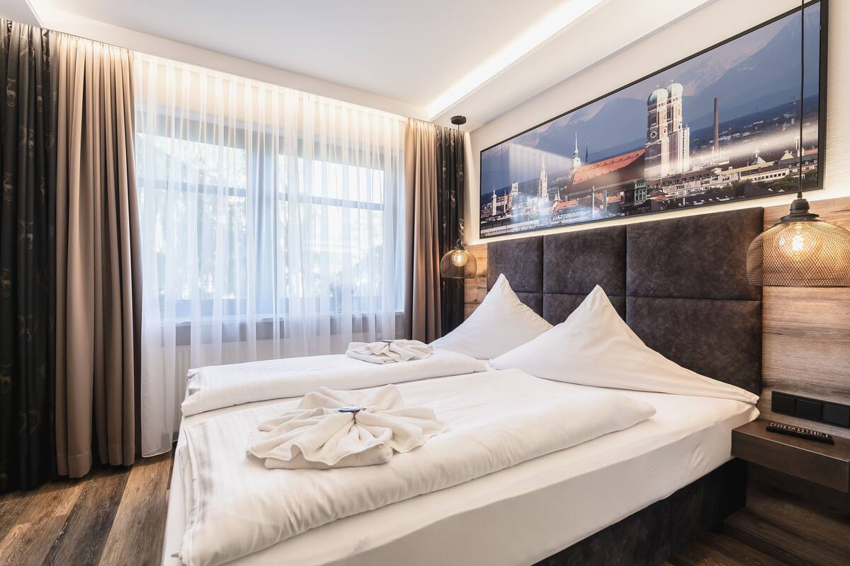 A hotel room with a large bed, a headboard, a nightstand, a lamp, and a cityscape view.