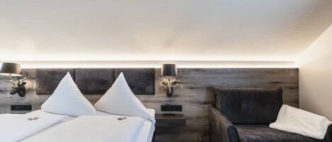 A modern bedroom with a bed, a dark armchair, and a headboard with wall-mounted lights.