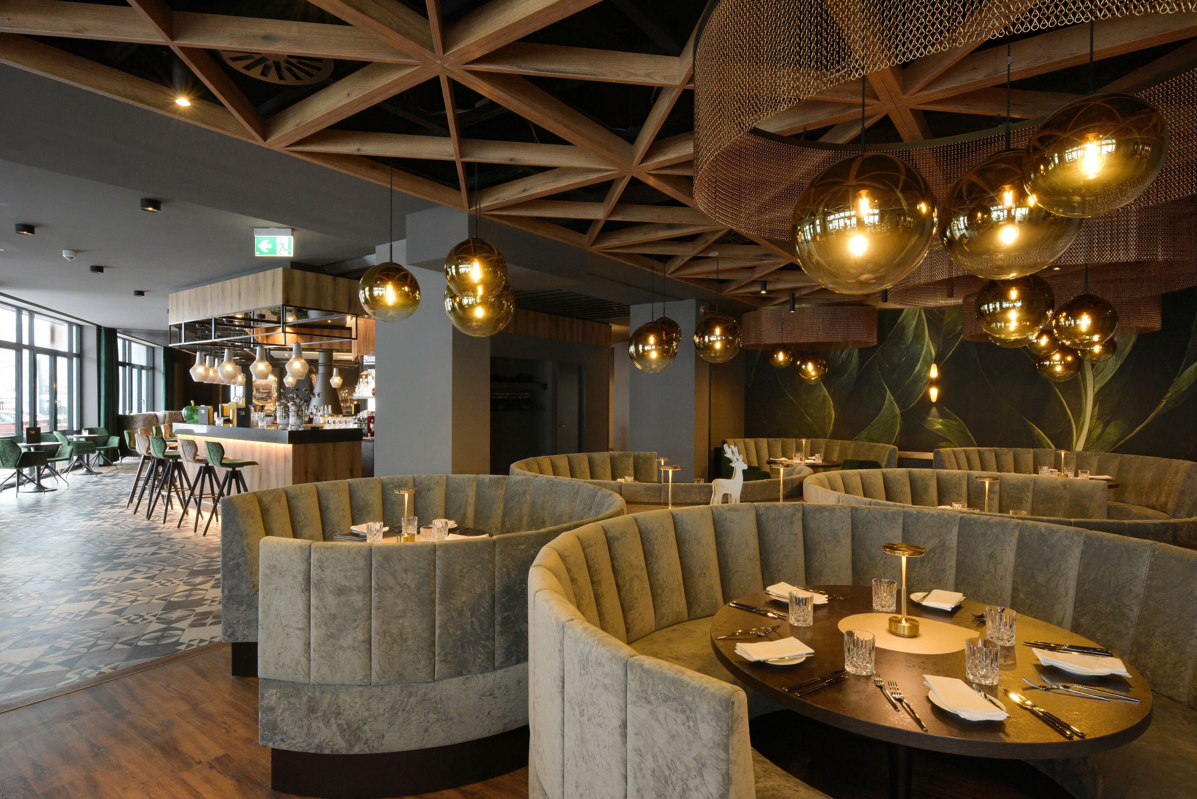 Un restaurant avec des tables rondes et des sièges rembourrés, un coin bar et de grandes fenêtres.