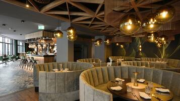 A restaurant with round tables and cushioned seating, a bar area, and large windows.